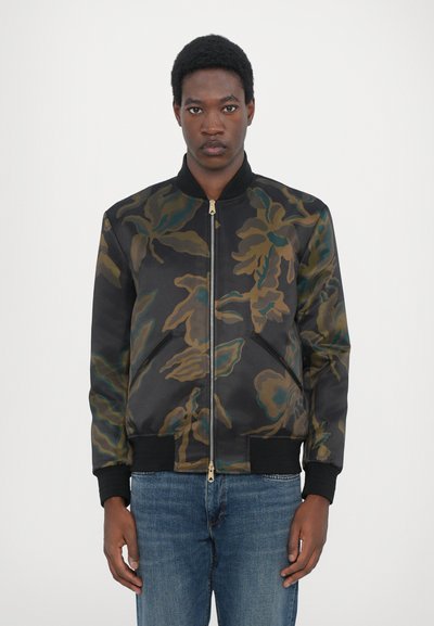 Giacca bomber camouflage con base nera, caratterizzata da motivi floreali verdi e marroni, polsini a coste e chiusura con zip frontale.