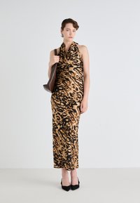 Leopardmønstret halterneck kjole i nuancer af brun og sort, knælang, fremstillet af et glat stof. Modellens holder en mørkebrun taske.