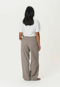 White short-sleeve shirt paired with high-waisted, wide-leg taupe pants featuring back pockets, smooth texture, and tailored design.