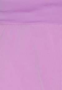 Světlé růžové tkaniny s hladkým povrchem, bezšvovým pasem a mírným leskem, navržené pro pohodlí a pružnost.