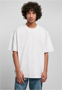 T-shirt bianco in cotone con vestibilità rilassata, maniche corte, scollatura rotonda e texture liscia, abbinato a jeans in denim blu chiaro.