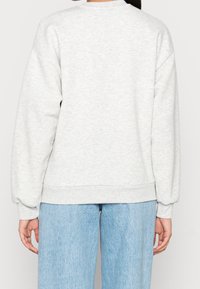 Sudadera gris con un acabado texturizado, que presenta un cuello y puños acanalados. Combinada con jeans de mezclilla azul claro.