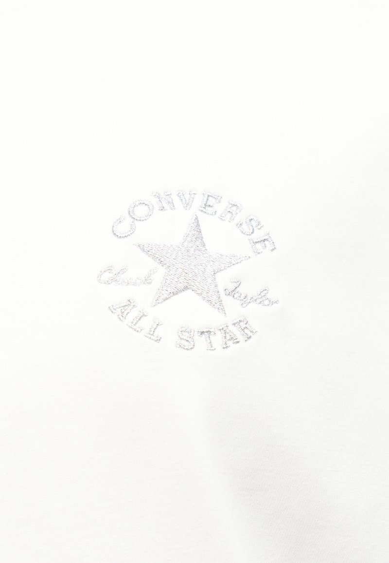 Tessuto bianco con logo Converse All Star ricamato tono su tono, che presenta una stella e un testo circostante.
