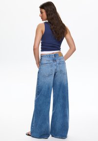 Jeans a gamba larga di colore azzurro chiaro realizzati in denim con una finitura sbiadita, dotati di due tasche posteriori e una toppa in pelle color cuoio in vita.