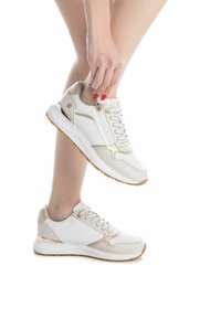Zapatillas deportivas blancas y doradas con diseño de cordones, detalles perforados y tobillo acolchado, con una suela de goma resistente.