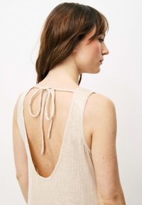 Ärmelloses beiges Kleid aus strukturiertem Stoff mit einem tiefen, offenen Rücken, der mit einem gebundenen Band gesichert ist. Minimalistisches Design und einfache Akzente.