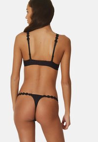 Set di lingerie nero composto da un bralette a righe con dettagli floreali sulle spalline e un tanga abbinato con dettagli in pizzo alla vita.