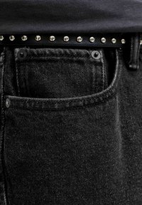 Zbliżenie na kieszeń czarnych dżinsów z czarną koszulą wpuszczoną do środka i czarnym paskiem z ćwiekami w pasie.