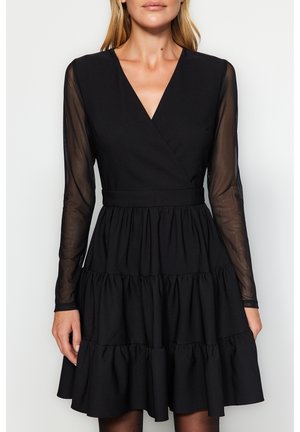 Schwarzes Wickelkleid mit langen, durchsichtigen Ärmeln, einem taillierten Oberteil und einem stufigen, gerafften Rock. Glatte Textur mit einem strukturierten Design.