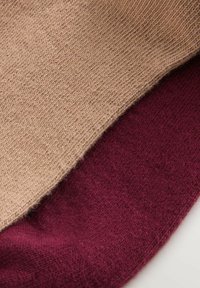 Tessuto a maglia in beige e bordeaux scuro, con una texture liscia e motivi di cucitura visibili, sovrapposti ai bordi.