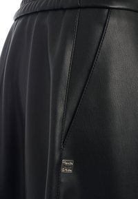 Shorts en cuir noir avec une texture lisse, comportant des coutures décoratives et une petite étiquette en métal sur le côté gauche.