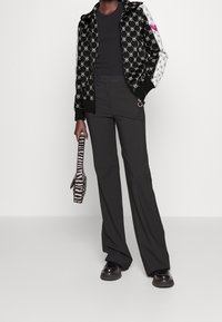 Black and white patterned hooded jacket with a zip, black fitted shirt, high-waisted trousers, and a striped bag. Black chunky shoes.