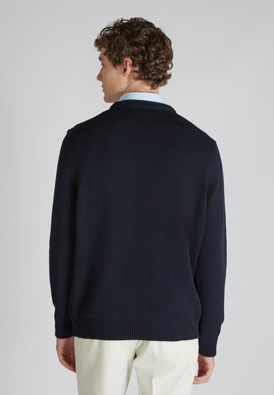 Granatowy sweter dzianinowy z prążkowanymi mankietami i dołem, o miękkiej fakturze i klasycznym kroju z kołnierzykiem, stylizowany z jasnymi spodniami.