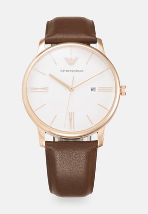Montre à bracelet en cuir marron avec un cadran blanc, un boîtier en acier rose en ton or, des index en chiffres romains et un affichage de la date à 3 heures.