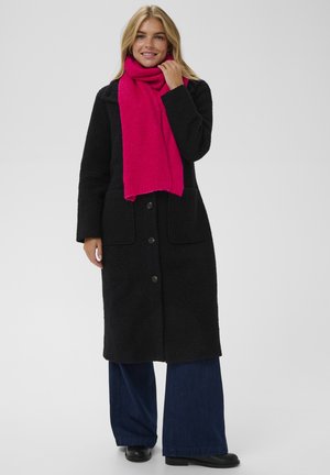 Black textured coat with button front, two large pockets, and a bright pink scarf. The model wears wide-leg blue jeans and black shoes.