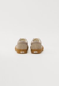 Baskets en daim beige avec une texture lisse, accents blancs et semelle en caoutchouc gomme. Logo Vans sur le talon, design bas.