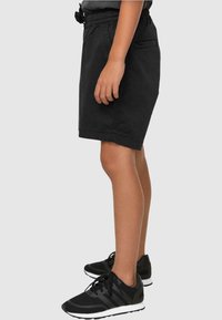 Shorts noirs avec une taille élastique et un cordon de serrage, des poches latérales et une coupe décontractée, associés à des baskets de sport noires.