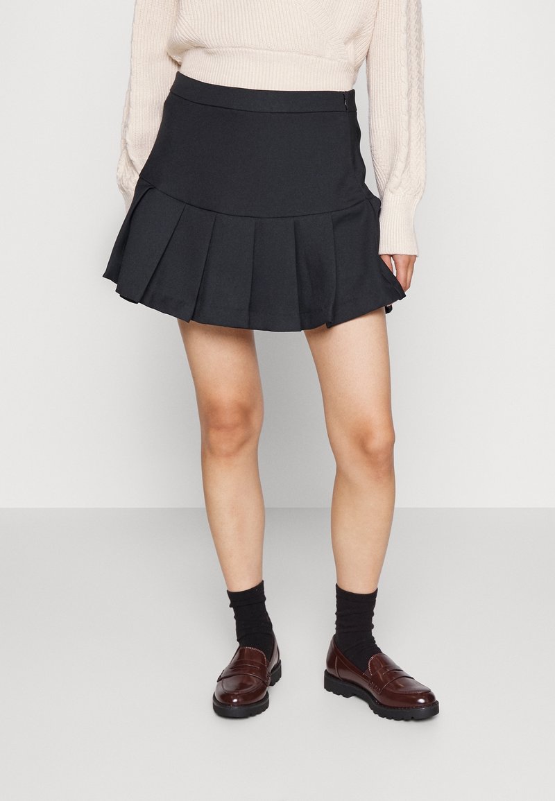 Musta, kangasta oleva pliseerattu minihame, jossa on istuva vyötärö ja sileä pinta. Yhdistetty tummien sukkien ja ruskeiden loaferien kanssa.