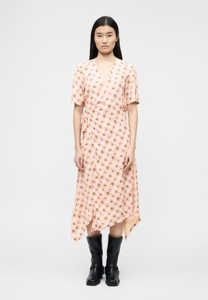 Kvinde iført en pink blomsterprint slå-om-kjole med korte ærmer og asymmetrisk skørt, kombineret med sorte læderstøvler til midt på læggen.