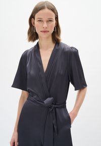 Giubbotto grigio scuro con maniche corte, design avvolgente e cintura con nodo auto-fissato in vita. Tessuto liscio con un motivo sottile e scollatura profonda.