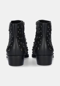 Botas de tobillo de cuero negro con remaches metálicos y cortes circulares. Con un tacón bajo y cremalleras laterales para facilitar su uso.