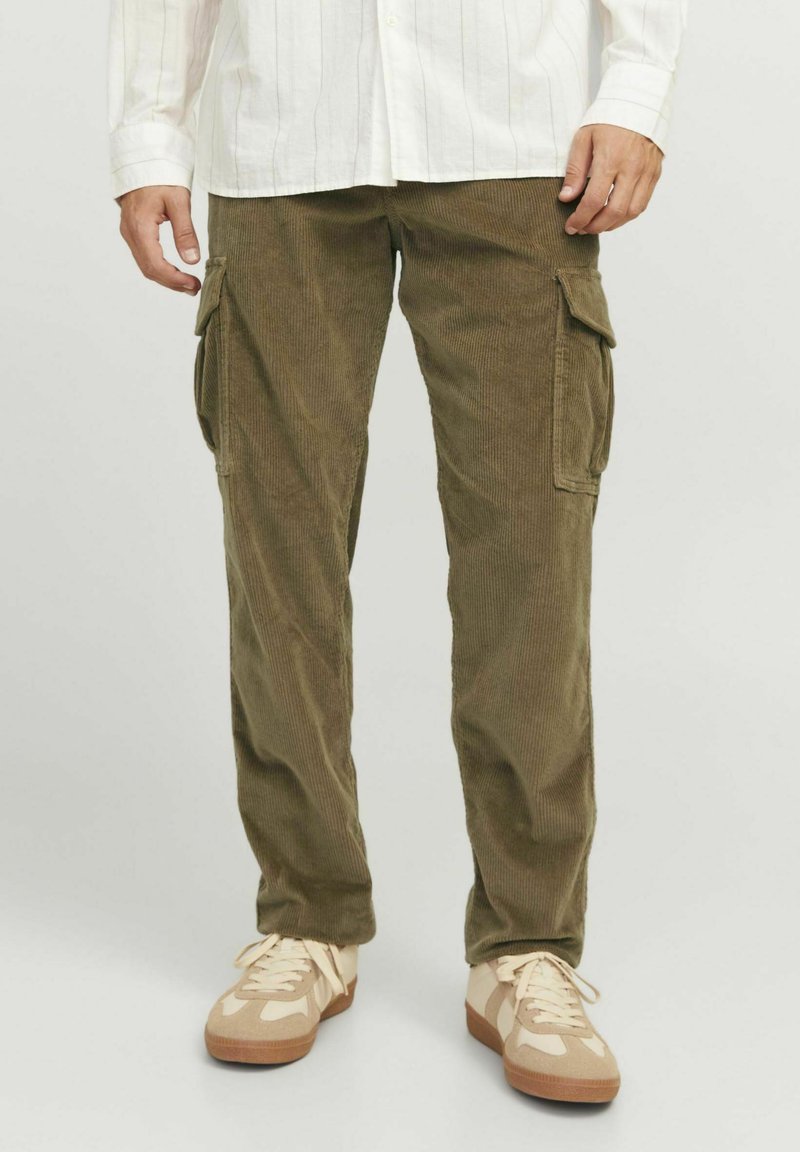 Un pantalon cargo en velours côtelé vert olive avec poches latérales, jambes droites et une texture douce, associé à des baskets beiges et une chemise blanche à boutons.