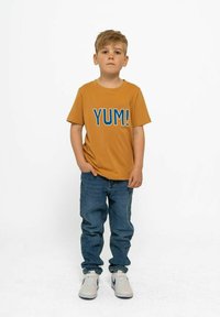 Tan spalvos trumpomis rankovėmis marškinėliai su mėlynu užrašu "YUM!", derinami su mėlynais džinsais ir baltais sportbačiais. Siluetas laisvas, su užlenktais rankovėmis.