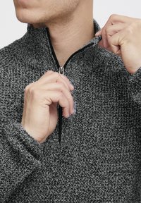 Grau und schwarz gemusterter Reißverschluss-Pullover mit hohem Kragen, ausgestattet mit einem glatten Reißverschluss und strukturiertem Strickstoff.
