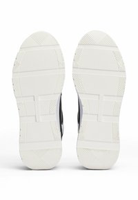 Schwarz-weiße Sohle von Sportschuhen aus strukturiertem Gummi, mit horizontalen und diagonalen Grip-Mustern und einer rein weißen farbigen Sohle.