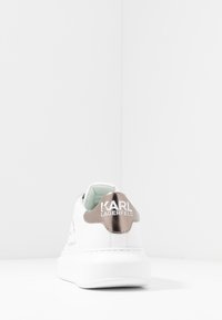 Valge sneake, millel on sile nahk, pehmendusega kaelus ja metallist roosa kuldne kannatugi, millel on "KARL LAGERFELD" brändi nimi.