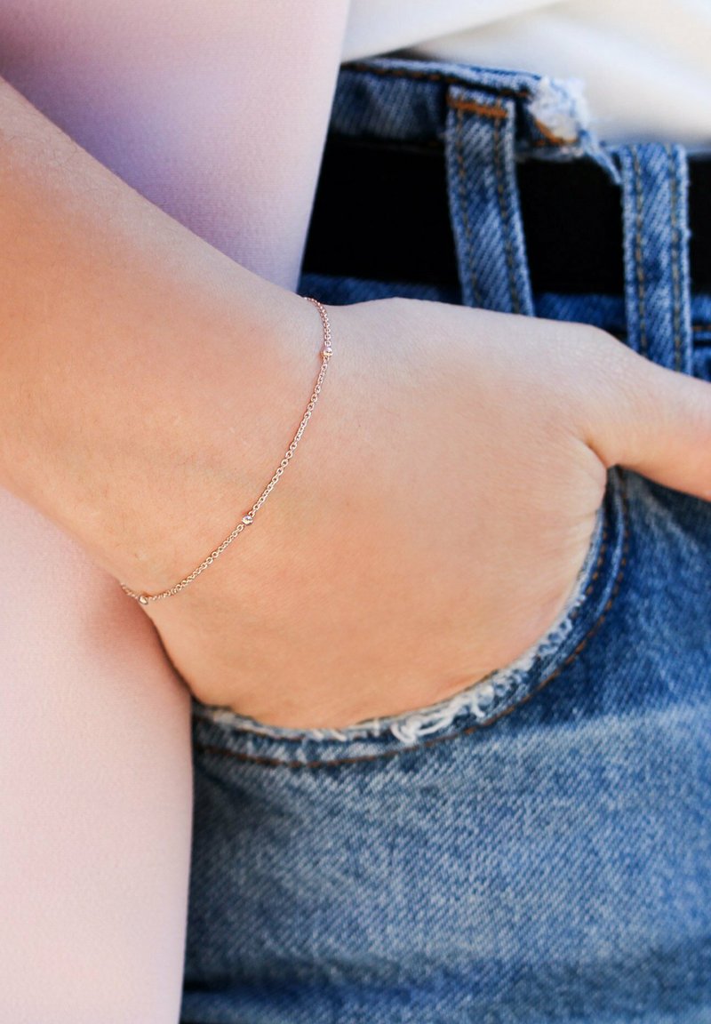 Mano con delicato braccialetto in catena d'oro che riposa all'interno della tasca di jeans blu vissuti.