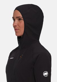 Black hooded jacket with a zippered front, featuring textured fabric, orange zipper pull, and white logo on the left sleeve.