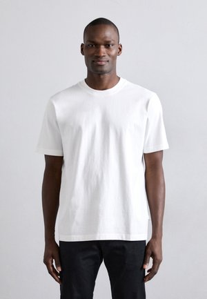 T-shirt bianco in cotone con maniche corte, scollatura rotonda e vestibilità rilassata. Orlo piatto e dettagli di cucitura minimali.