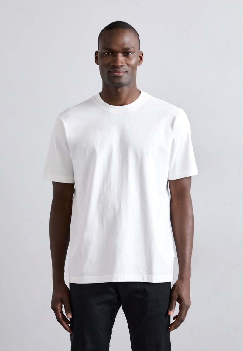 Camiseta de algodón blanca con mangas cortas, escote redondo y corte relajado. Dobladillo plano y detalles de costura mínimos.