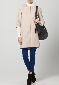 Beige zippered coat with short sleeves, paired with a white blouse and blue pants. Accessories include a black bag and black ankle boots.