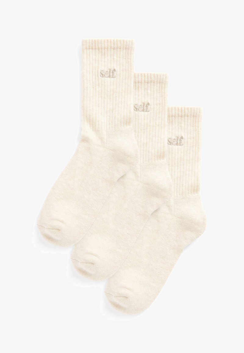 Three pairs of cream-colored ribbed socks made from soft material. Each sock features a small embroidered "self" logo near the cuff.