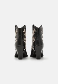 Botas de cuero negro hasta el tobillo con tacones afilados, que presentan un patrón de hojas en beige en los lados y una textura suave.