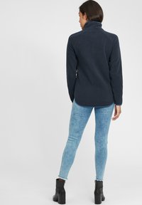 Tengerészeti fleece pulóver magas gallérral, puha tapintású és ívelt hem. Világoskék skinny farmerral és fekete bokacsizmával párosítva.