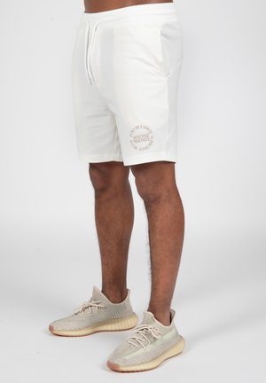 Hvide bomuldsshorts med sidelommer, med et rundt tekstdesign i lysebrun. Kombineret med beige sneakers.
