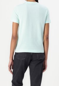 Mintgrøn kortærmet t-shirt med rund hals, lavet af blødt stof; parret med mørkegrå jeans med to baglommer.