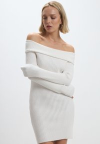 Abito dolce vita bianco a coste con scollo a spalle scoperte e maniche lunghe, caratterizzato da una silhouette aderente e una morbida texture.