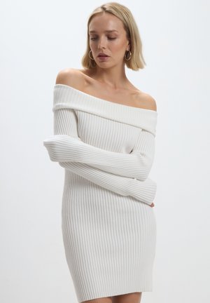 Abito dolce vita bianco a coste con scollo a spalle scoperte e maniche lunghe, caratterizzato da una silhouette aderente e una morbida texture.