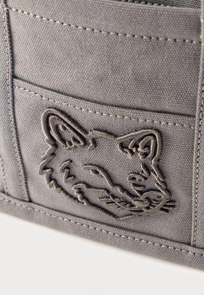 Κοντινό πλάνο μιας τσέπης από γκρι ύφασμα με ραμμένο περίγραμμα προσώπου γάτας στην επιφάνειά της.