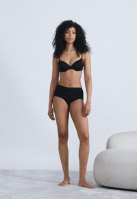 Μαύρο σουτιέν με ενίσχυση και ταιριαστό σορτς με ψηλή μέση, το μοντέλο πόζαρε σε ανοιχτό γκρι φόντο. Απαλή υφή, λιτός σχεδιασμός.