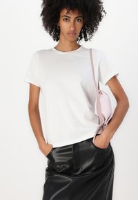 Hvid t-shirt med korte ærmer i blødt stof, parret med en blank sort faux læder nederdel og en lille lyserød crossover taske.