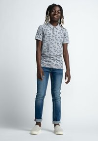 Šedé polo tričko se vzorem černých palem, krátké rukávy. V kombinaci s modrými džíny a bílými slip-on botami. Jednoduchý, ležérní design.