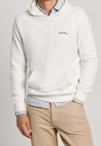 Felpa bianca con cappuccio, tasca frontale e polsini a costine, con un piccolo logo nero "Pepe Jeans" sul petto, indossata sopra una camicia azzurro chiaro.
