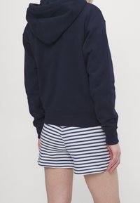 Marinblå huvtröja med texturerad tyg, kombinerad med krämfärgade och marinblå randiga shorts. Synliga sömdetaljer och ribbade ärmslut.