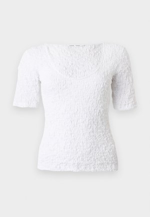 Biała teksturowana bluzka z krótkim rękawem, o dekolcie w łódkę i dopasowanym kroju na neutralnym tle.