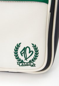 Borsa in tela bianca con accenti verdi, caratterizzata da un logo ricamato, foglie di alloro e bordi blu navy. Forma rettangolare elegante con superficie testurizzata.
